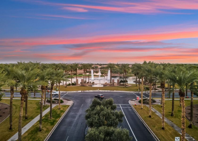 A road with palm trees and a building in the background.