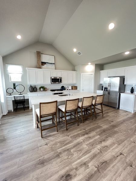 Spacious kitchen with vaulted ceilings, white cabinetry, and wood floors, featuring an island and wicker stools.