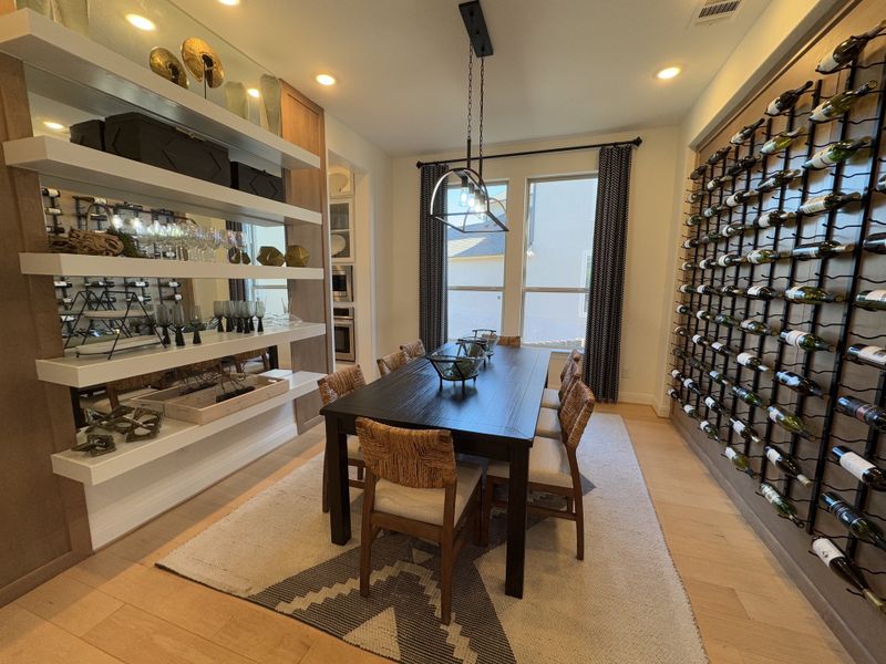 A chic dining room featuring a sleek table, wine storage wall, modern shelves, and warm lighting. A chic dining room featuring a sleek table, wine storage wall, modern shelves, and warm lighting.