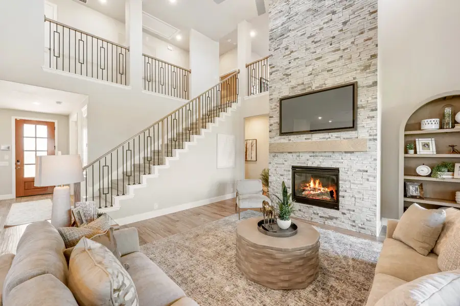 Open living room with two-story ceiling, stone fireplace, staircase, and built-in shelving Open living room with two-story ceiling, stone fireplace, staircase, and built-in shelving