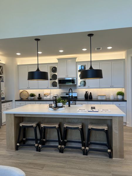 A modern kitchen with sleek pendant lights, white cabinetry, an island with stools, and light wood flooring.