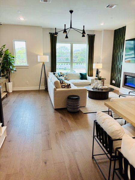 A modern living room featuring a beige sectional, sleek lighting, and wooden floors, accented with natural light and greenery.