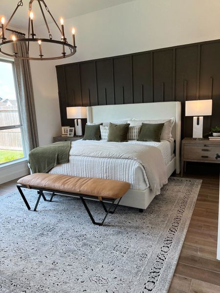 A modern bedroom featuring a dark accent wall, elegant chandelier, cozy bed, and chic decor.