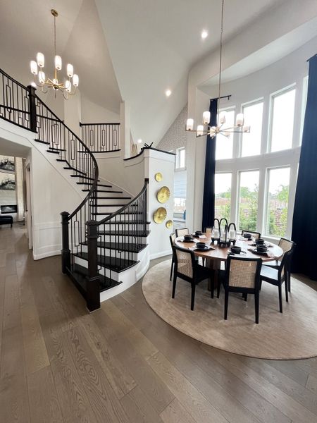 A modern dining area with a round table, elegant staircase, and large windows, creating an inviting ambiance.