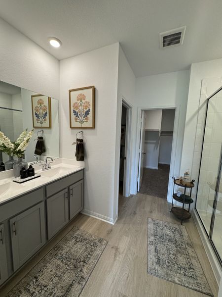 A modern bathroom featuring dual sinks, elegant gray cabinetry, and sleek wood flooring.