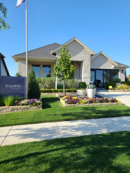 Charming brick home with lush landscaping at Painted Tree by Tri Pointe Homes (McKinney, TX).