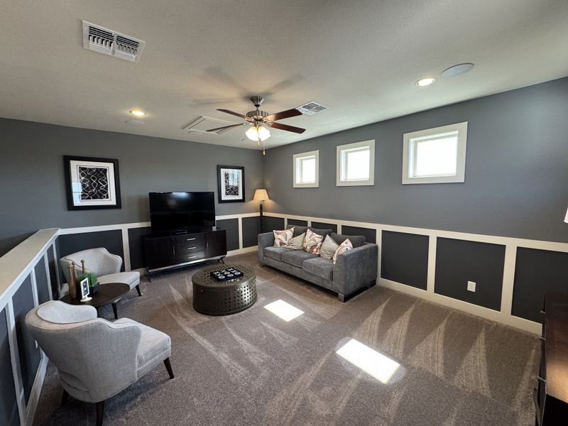 A cozy living room featuring gray walls, plush seating, wall art, and a modern ceiling fan, creating a stylish and inviting space.