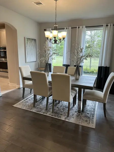 A cozy dining area with elegant cream chairs, a wooden table, and a chic chandelier overlooking a lush view. A cozy dining area with elegant cream chairs, a wooden table, and a chic chandelier overlooking a lush view.