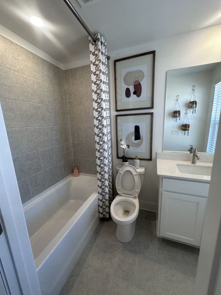 A modern bathroom featuring gray tile, a sleek white vanity, and abstract wall art.
