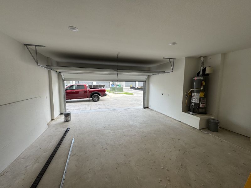 A spacious garage with a concrete floor, open door, and water heater, offering ample storage and utility.