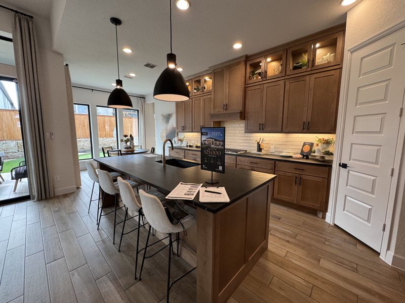 A spacious kitchen with wooden cabinetry, black countertops, pendant lighting, and a large island with seating and garden views.