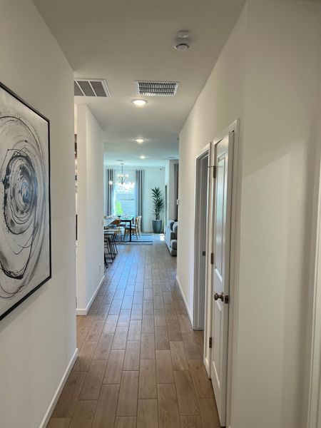 A sleek hallway with wood floors, modern art, and recessed lighting leads to an open living area with dining space.