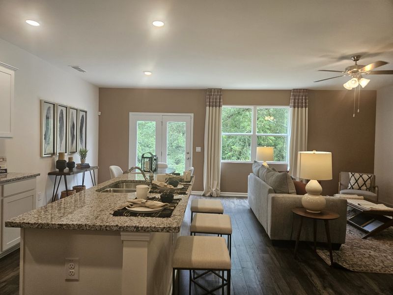 A modern open-plan space featuring a granite kitchen island, cozy living area, and large windows overlooking greenery. A modern open-plan space featuring a granite kitchen island, cozy living area, and large windows overlooking greenery.