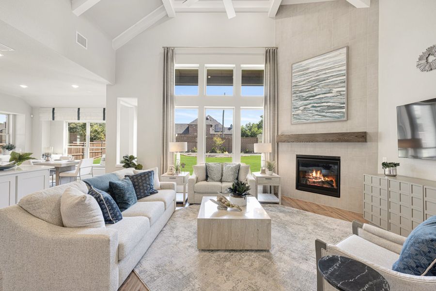 Bright living room with vaulted coffered ceiling, tile fireplace, large windows, and neutral furniture with blue accent pillows