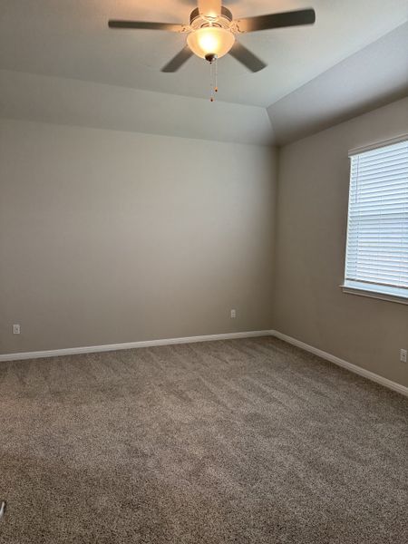 A spacious bedroom featuring plush carpet, neutral walls, and a ceiling fan, enhanced by natural light from large windows.