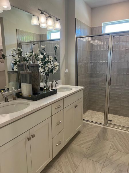 Elegant bathroom with dual sinks, light cabinetry, and a glass shower. Bright tiles complete the modern look.