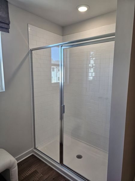A sleek, modern shower with glossy subway tiles and a glass door, bathed in natural light. A sleek, modern shower with glossy subway tiles and a glass door, bathed in natural light.