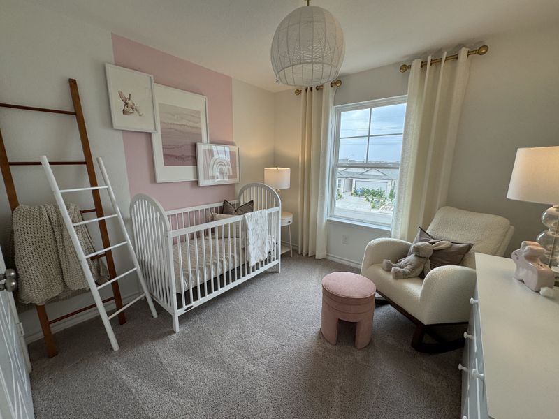 A cozy nursery with a soft armchair, white crib, pink accents, and playful wall art creates a serene and welcoming atmosphere.