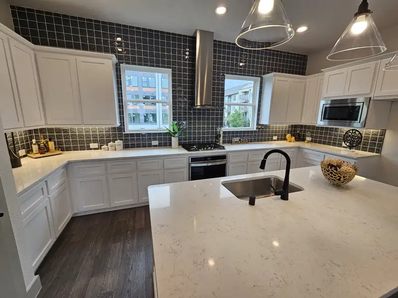 A modern kitchen with dark tiled backsplash, sleek white cabinetry, and a spacious island with pendant lighting.
