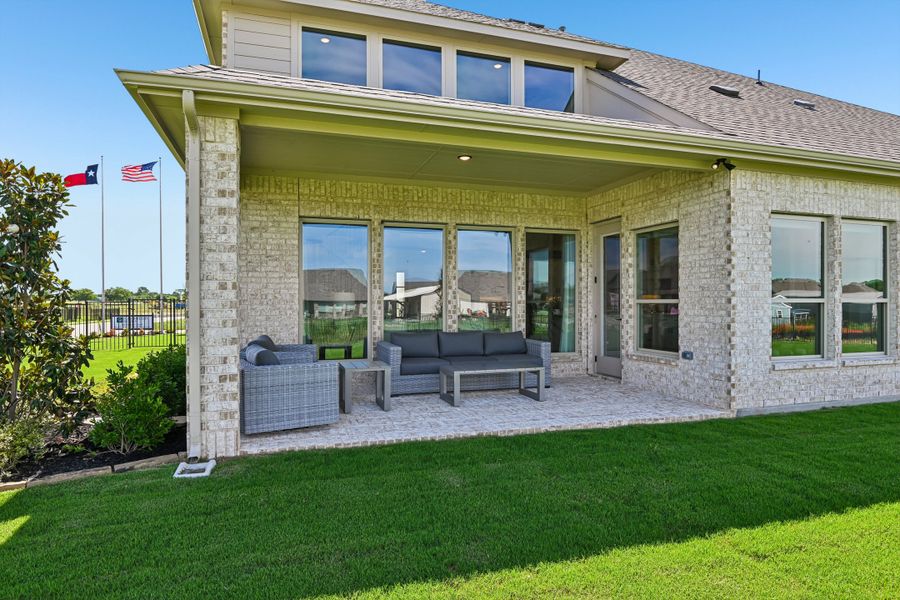 Covered back patio with gray wicker seating set on brick home with green lawn and Texas flag visible. Covered back patio with gray wicker seating set on brick home with green lawn and Texas flag visible.