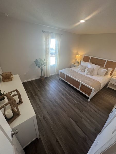 A cozy bedroom with a wooden floor, elegant bed, soft lighting, and sheer curtains creating a serene atmosphere.