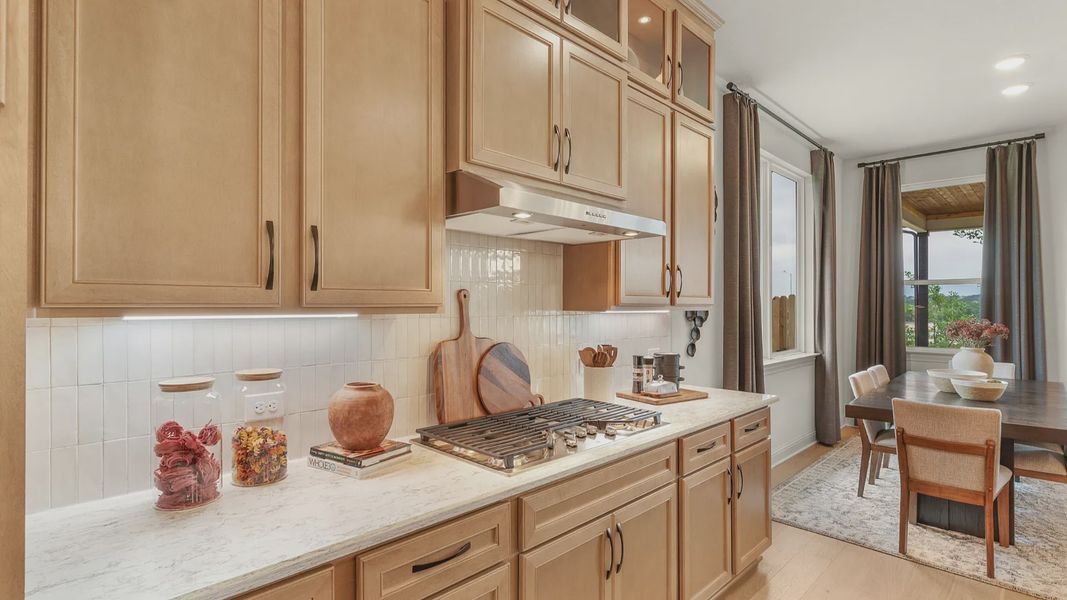 Kitchen features a stainless vent hood, cabinet accent lighting, and a sleek gas cooktop.