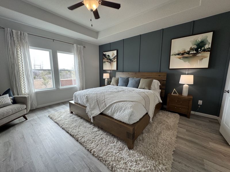 A cozy bedroom featuring a wooden bed, plush rug, abstract art, and elegant natural light from large windows.