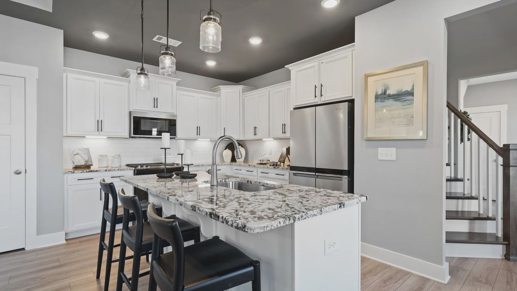 Kitchen at Village at Midway by DRB Homes with modern accents, dark ceiling, granite countertops, and white cabinetry Kitchen at Village at Midway by DRB Homes with modern accents, dark ceiling, granite countertops, and white cabinetry