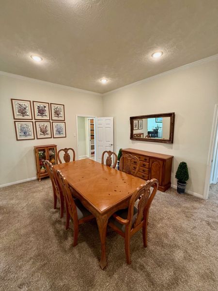 An elegant dining room featuring a wooden table set, plush carpet, and classic art pieces adorning the walls.