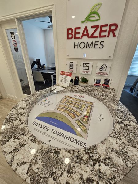 A modern sales center desk with a Bayside Townhomes map and Beazer Homes signage.