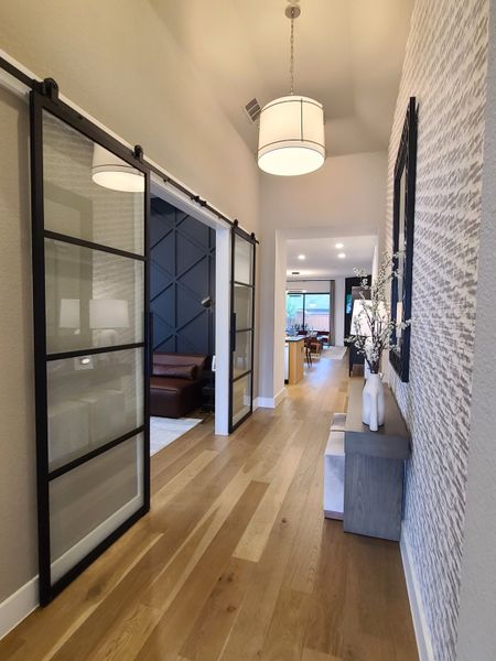 A modern hallway with sliding glass doors, textured accent wall, and warm wood flooring, leading to an inviting living area.