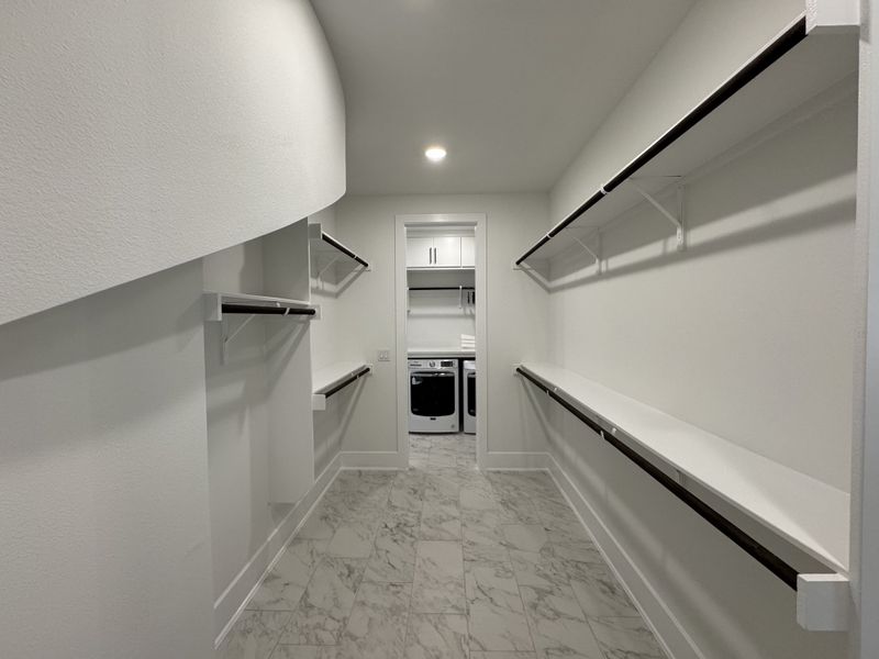A spacious walk-in closet with sleek shelving and a marble-look floor, leading to a convenient laundry area.