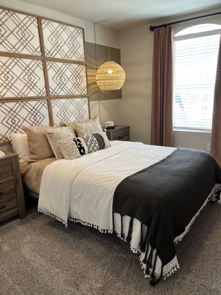 A cozy bedroom with a patterned accent wall, textured bedding, and a warm woven pendant light.