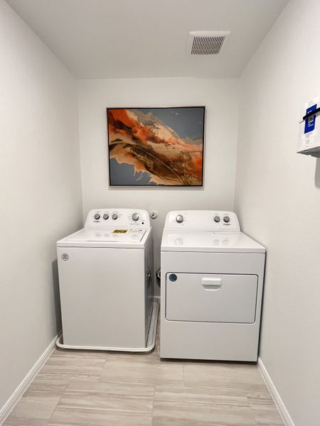A modern laundry room featuring a washer, dryer, abstract artwork, and sleek tile flooring. A modern laundry room featuring a washer, dryer, abstract artwork, and sleek tile flooring.