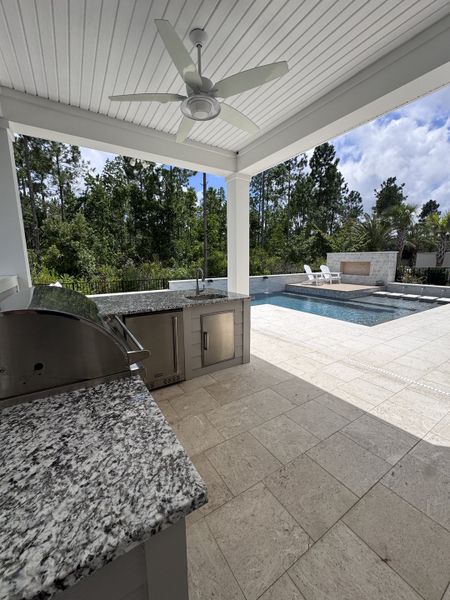 A luxurious outdoor kitchen with granite countertops, ceiling fan, and a pool view. Perfect for entertaining and relaxation. A luxurious outdoor kitchen with granite countertops, ceiling fan, and a pool view. Perfect for entertaining and relaxation.