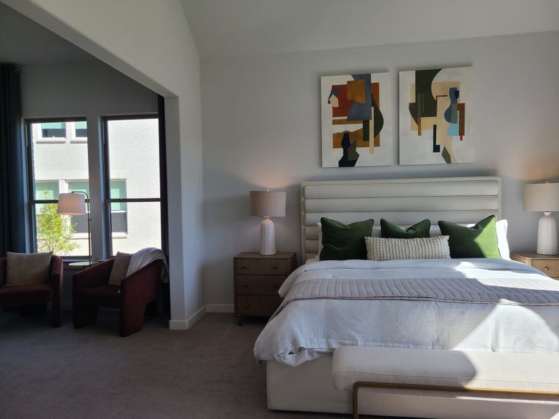 A serene and modern bedroom with abstract art, plush bedding, and cozy seating area by the window.