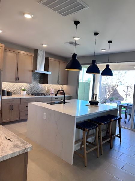 A contemporary kitchen with a sleek marble waterfall island, wood cabinetry, and stylish black pendant lighting.