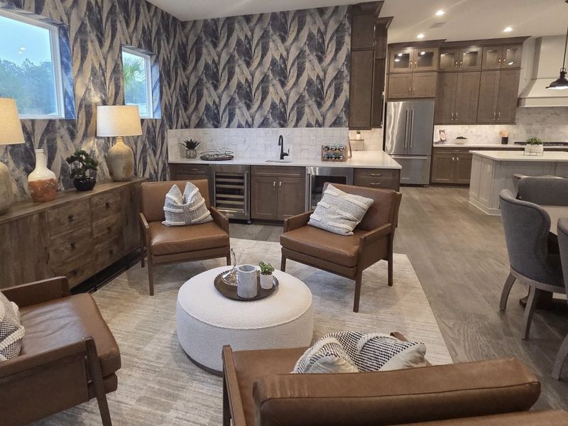 A cozy living area with leather chairs, modern wallpaper, and an open kitchen, creating a warm, stylish ambiance.