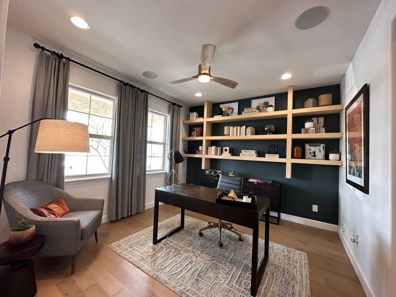 A modern home office with sleek shelving, a stylish desk, and cozy seating under soft lighting and elegant curtains.