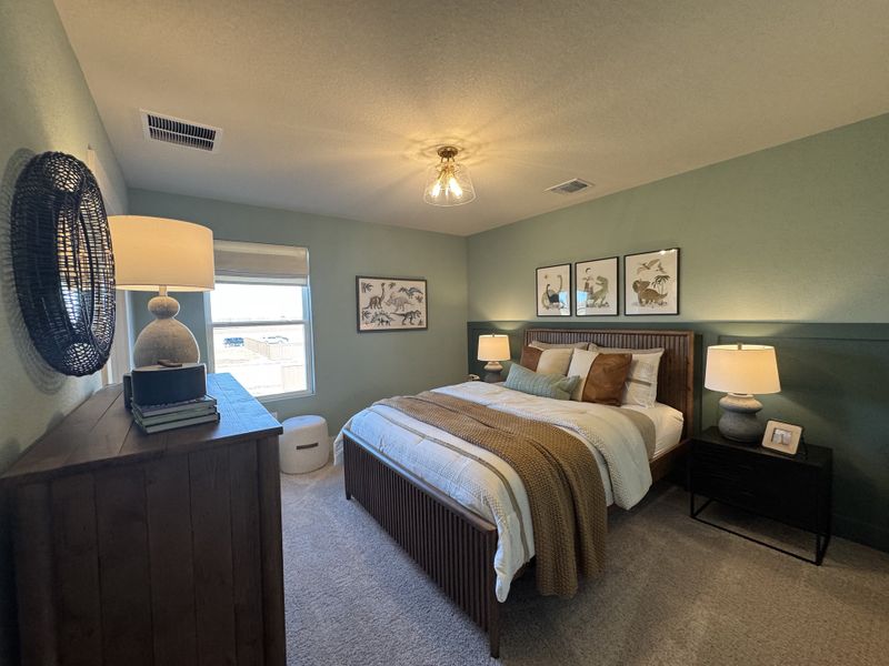 Cozy bedroom with soft green walls, plush bedding, and warm lighting, enhanced by elegant artwork and a rustic wooden dresser.