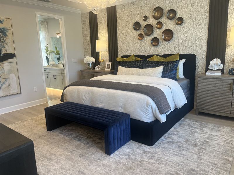 A chic bedroom with textured wallpaper, elegant decor, a plush bed, and a cozy bench, seamlessly leading to a bright bath. A chic bedroom with textured wallpaper, elegant decor, a plush bed, and a cozy bench, seamlessly leading to a bright bath.