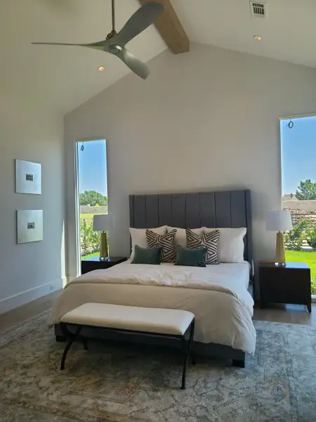 A serene bedroom featuring a plush gray headboard, elegant decor, and large windows for ample natural light.