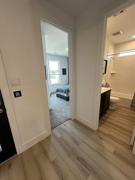 A cozy hallway with wood flooring leads to a bright bedroom and a modern bathroom featuring white subway tiles.