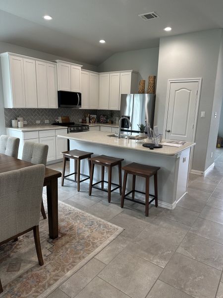 A modern kitchen with white cabinetry, stainless steel appliances, and a cozy dining area with a stylish rug and bar stools. A modern kitchen with white cabinetry, stainless steel appliances, and a cozy dining area with a stylish rug and bar stools.