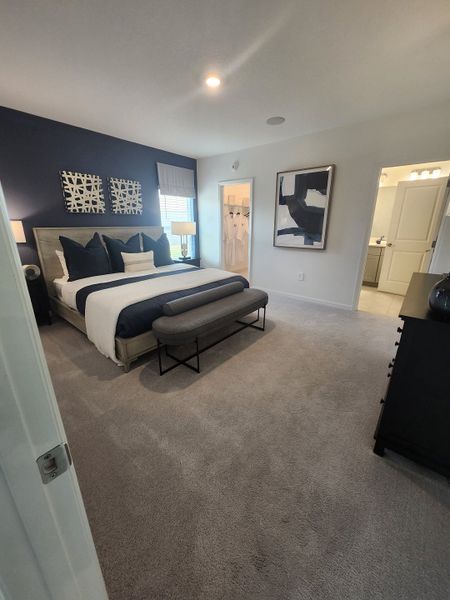 A cozy bedroom with a dark accent wall, stylish bedding, and modern art. Carpeted floor leads to a sleek bath and walk-in closet.