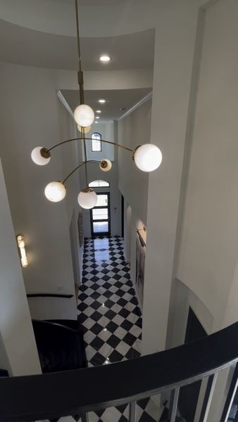 A grand hallway featuring black-and-white checkered flooring and a modern chandelier with globe lights.