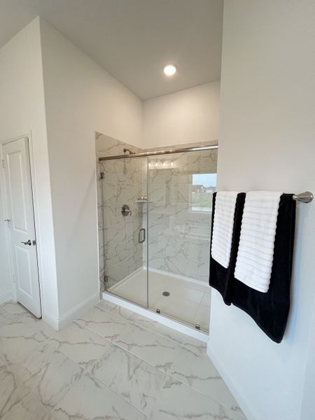 A modern bathroom featuring marble tile, a sleek glass shower, and elegant towel accents for a luxurious feel.