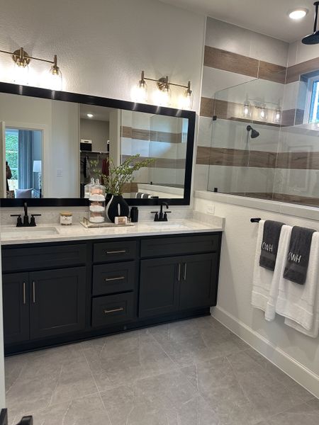 A modern bathroom with a sleek black vanity, spacious mirror, and elegant lighting, complemented by gray tiled flooring.