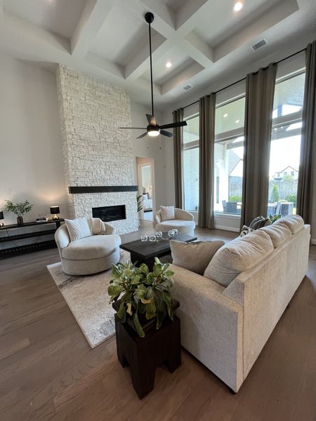 A bright, elegant living room with a stone fireplace, cozy seating, and floor-to-ceiling windows for abundant natural light.