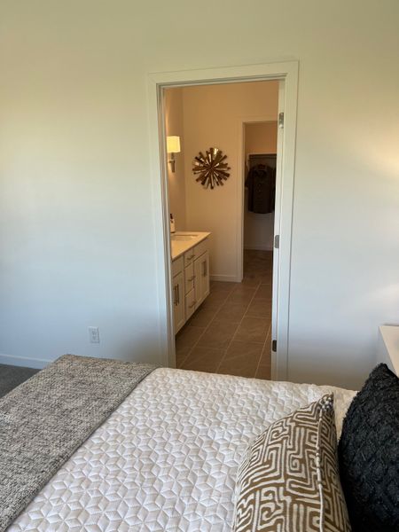 Cozy bedroom with stylish quilt and patterned pillows, leading to a chic bathroom with modern decor and ample storage.